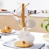 A wooden mug tree with white mugs on it, placed on a kitchen counter with donuts in the foreground. Produktbild-Vorschau