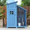 A blue wooden garden shed with a slanted roof, standing on a patio in front of a wooden fence. Gardening tools are stored inside the open section of the shed. Voir les images du produit