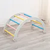 A wooden climbing arch for children, set up indoors on a wooden floor against a white wall. Voir les images du produit