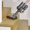 A person is vacuuming a wooden staircase with a cordless stick vacuum cleaner. Produktbild-Vorschau