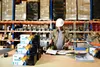 A warehouse worker in a hard hat is standing at a table with several boxes of toner cartridges. Produktbild-Vorschau