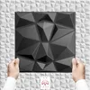Hands holding a black 3D wall panel in front of a white textured wall. Produktbild-Vorschau