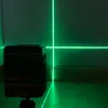 A laser level projects green lines on a wall and floor in a dimly lit room, with the device visible in the foreground. Náhľad obrázku produktu