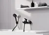 A black shower head and faucet are mounted on a white tiled wall above a bathtub. Anteprima dell’immagine prodotto