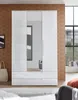 A white, high-gloss wardrobe with three doors and two drawers, featuring a full-length mirror on the middle door. The wardrobe is set in a room with a textured brown wall and a window in the background. A white tote bag is visible to the left of the wardro Produktbild-Vorschau