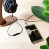 A pair of headphones connected to a smartphone displaying an audio waveform, placed on a wooden surface next to a plant. Produktbild-Vorschau