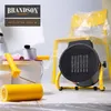 A black and yellow heater is placed on a tiled floor next to painting supplies, with a yellow chair covered in plastic wrap in the background. Náhled obrázku produktu