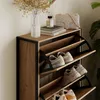 A shoe cabinet with shoes stored inside, placed next to a wall with decorative items. Anteprima dell’immagine prodotto