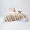 A neatly made bed with white sheets and a striped throw blanket and pillows. Náhled obrázku produktu