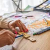 A person's hands are shown coloring in a book with colored pencils. Produktbild-Vorschau