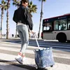 A woman is walking across a crosswalk with a shopping trolley, a bus is passing by. Produktbild-Vorschau