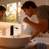 A man brushing his teeth in a bathroom with a modern sink and faucet. Produktbild-Vorschau