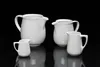Four white ceramic pitchers of varying sizes are arranged on a reflective black surface against a black background. Anteprima dell’immagine prodotto