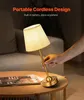 A hand is adjusting a portable cordless table lamp on a wooden coffee table next to a sofa. A magazine is also on the table. Produktbild-Vorschau