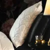 A close-up of a quilted pillow resting on a black leather surface, with a glass and a candle holder on a small table in the foreground. Produktbild-Vorschau