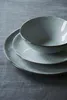 A stack of three ceramic dishes with a striped pattern on a gray fabric surface. Produktbild-Vorschau