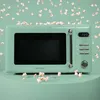 A retro-style mint green microwave oven is shown on a light green surface, surrounded by scattered popcorn. Náhľad obrázku produktu