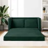A dark green sofa bed is laid out flat on a rug in a room with a large plant and a bookshelf in the background. Produktbild-Vorschau