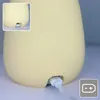 Close-up of the bottom of a yellow silicone night light, showing a USB charging port with a white cable plugged in. A small inset shows a detail of the charging port. Podgląd zdjęcia produktu