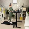 A woman is working on a laptop while standing on a treadmill in a home office. Produktbild-Vorschau
