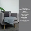 A grey armchair with a blue fleece blanket draped over it, next to a plant. Produktbild-Vorschau