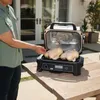 A person is using an electric grill outdoors on a wooden table, with two whole chickens on the grill. Voir les images du produit