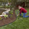 A woman is installing black garden edging around a flower bed next to a pond. Produktbild-Vorschau