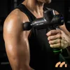 A person is using a massage gun on their shoulder in a gym setting. Produktbild-Vorschau
