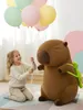 A young girl is holding balloons next to a large capybara plush toy. Produktbild-Vorschau