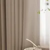 A close-up view of a khaki-colored curtain with vertical pleats, next to a window with sheer white curtains. A small plant branch is visible to the right. Produktbild-Vorschau