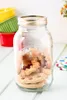 A glass jar filled with cookies sits on a light-colored wooden surface, with colorful ramekins in the background. Podgląd zdjęcia produktu
