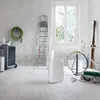 A white dehumidifier is placed on a white wooden floor in a room with various items like a ladder, bicycle, and storage unit. Voir les images du produit