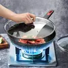 A hand is shown placing a glass lid on a wok filled with shrimp, which is cooking on a gas stove. Produktbild-Vorschau
