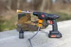 A cordless pressure washer with accessories is placed on a concrete surface next to a hiking boot, with a blurred outdoor background. Náhled obrázku produktu