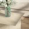 A close-up shot of a travertine coffee table with a vase of flowers on it, placed next to a sofa. Náhled obrázku produktu
