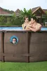 A couple is relaxing in an above-ground pool, while a child peeks out from a window in the pool wall. Produktbild-Vorschau