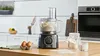 A Bosch food processor is shown on a kitchen counter with ingredients like eggs and flour nearby. Produktbild-Vorschau