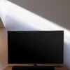 A television set and soundbar are placed on a wooden surface in front of a wall with angled lighting. Anteprima dell’immagine prodotto