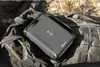 A gray power bank with a wireless charging symbol is placed on a green backpack. Produktbild-Vorschau