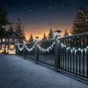 A snowy night scene with a house decorated for Christmas, a fence with lights, and Christmas trees. Voir les images du produit