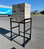 A metal stand holding a stack of concrete pavers, with an Amazon truck in the background. Produktbild-Vorschau