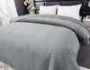 A close-up view of a gray quilted bedspread with a chevron pattern, draped over a bed with white pillows and a black headboard. Podgląd zdjęcia produktu