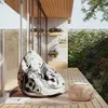 A bean bag chair with a football design sits on a wooden deck next to a small round table, with plants and a stone wall in the background. Voir les images du produit