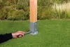 A hand using a wrench to secure a wooden post in a metal ground socket on a lawn. Produktbild-Vorschau