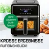 A black air fryer with fries inside, set against a blurred kitchen background and a pile of fried chicken. Anteprima dell’immagine prodotto