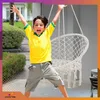 A young boy is jumping with excitement in front of a white macrame hanging chair. Produktbild-Vorschau