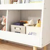 A close-up view of a white children's bookshelf with toys and books stored inside. The bookshelf has wooden legs and is placed on a wooden floor. Náhľad obrázku produktu