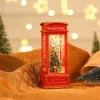 A festive Christmas-themed telephone booth decoration with a lit Christmas tree inside, placed on a burlap-like surface with blurred bokeh lights in the background. Náhled obrázku produktu