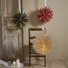 Three decorative paper stars are hanging, one on a vintage door, one on a chair, and one on the wall. Candles are lit in the foreground. Podgląd zdjęcia produktu