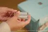 Hands holding a battery pack with two AA batteries inside, with a light blue box in the background. Anteprima dell’immagine prodotto